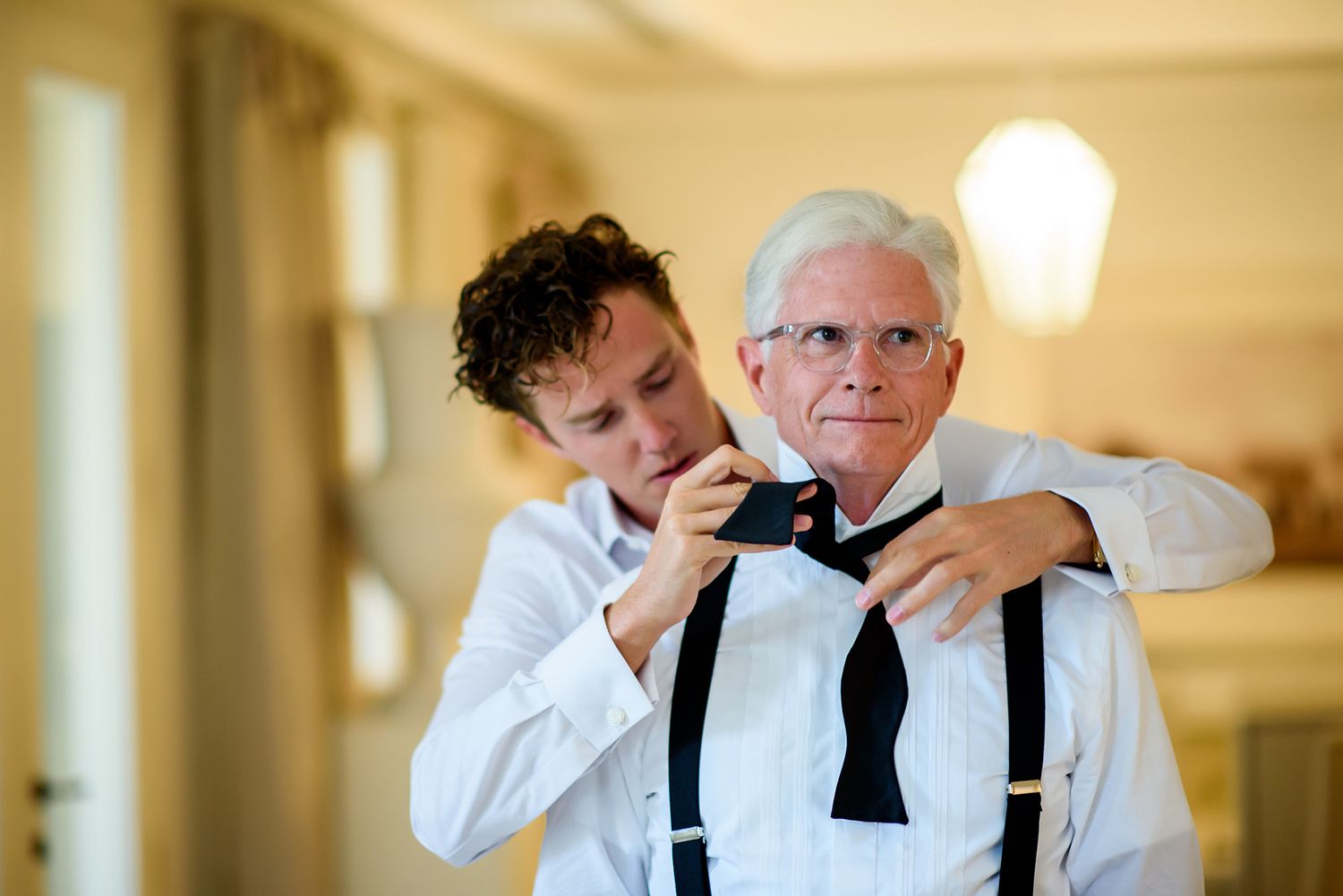 Men adjusting ties and suspenders while getting ready in a bright interior space.
