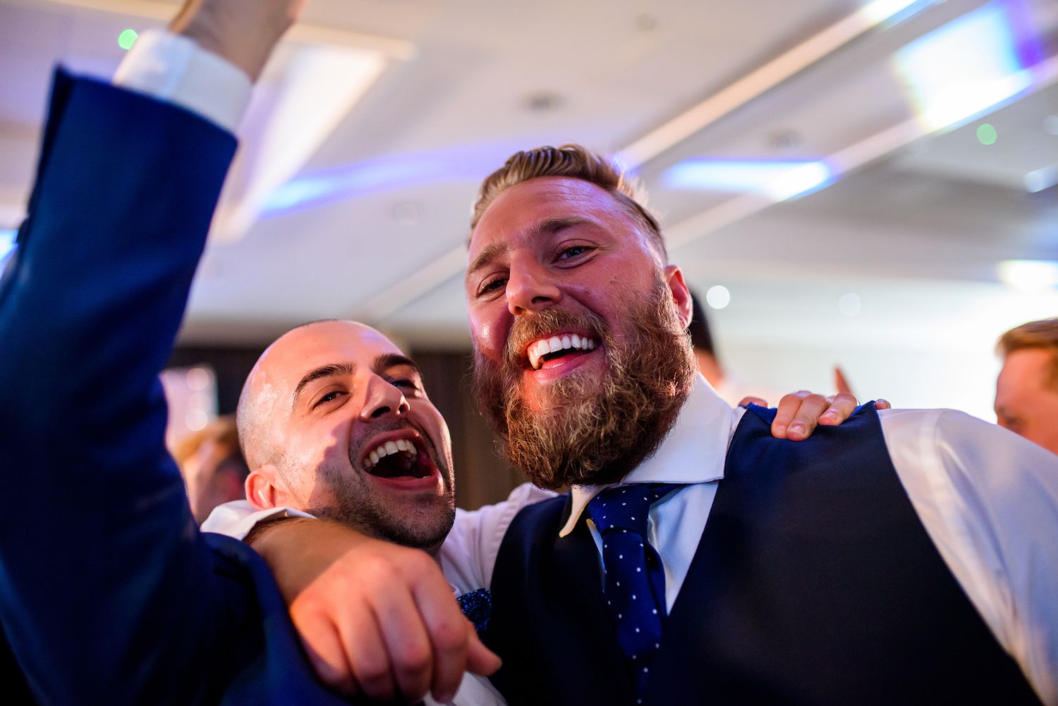 Candid black and white photo of guests laughing and celebrating at a wedding reception.