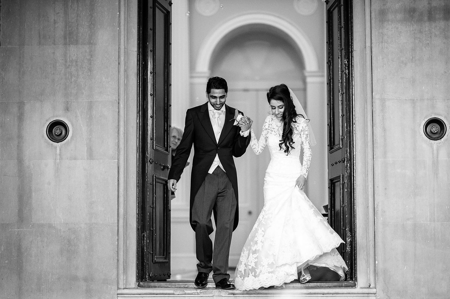 Black and white photo of newlyweds exiting through arched doorway.