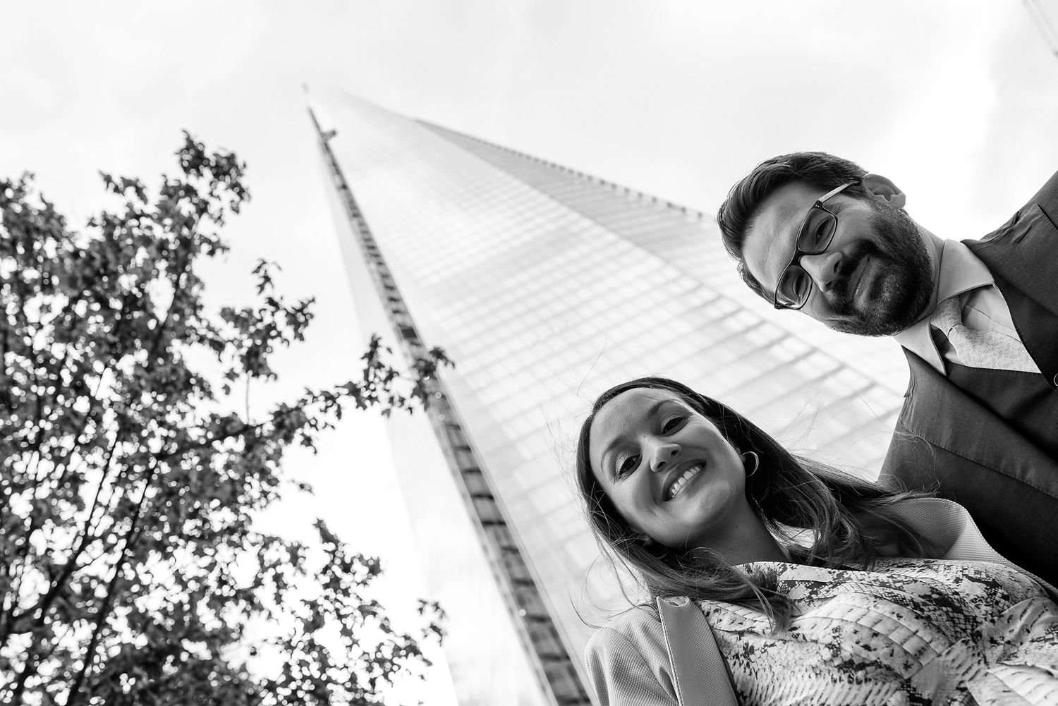 Looking up view of couple laughing together against blue sky and tall buildings.