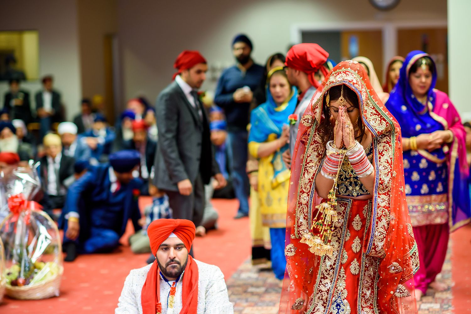 Sikh wedding ceremony with bride and groom participating in traditional rituals on red carpeted floor.