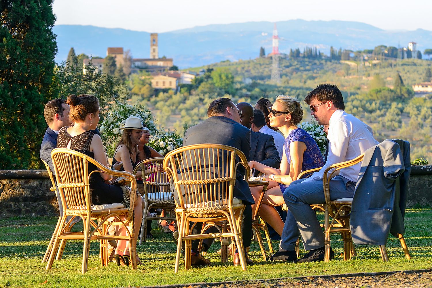Wedding guests relaxing in outdoor chairs overlooking the Tuscan countryside at sunset.