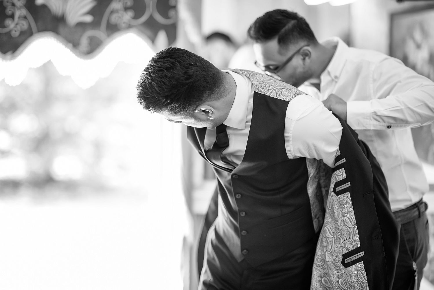 Black and white photograph showing wedding day preparation with formal attire adjustments.
