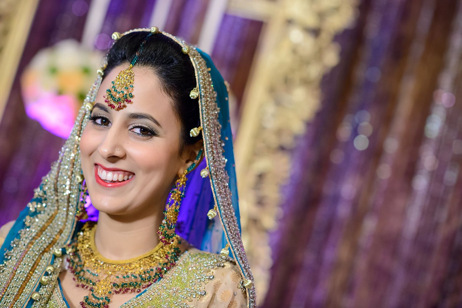 Traditional South Asian bride wearing glittering turquoise and gold bridal attire with ornate jewelry.