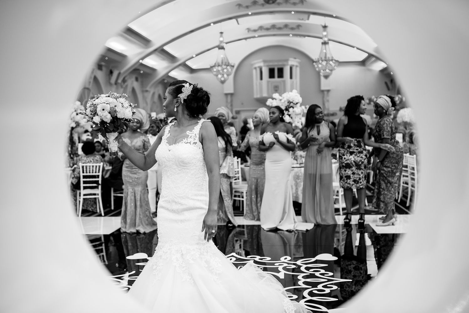 Black and white photo of wedding guests watching the celebration through a circular mirror frame.