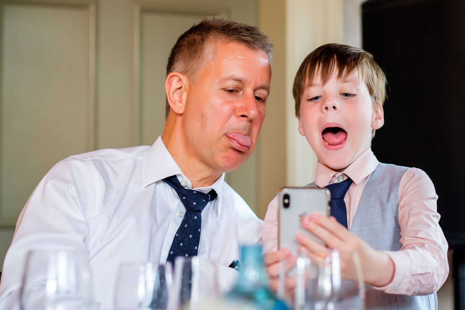 A parent and child look at a mobile device together with animated expressions during a meal.