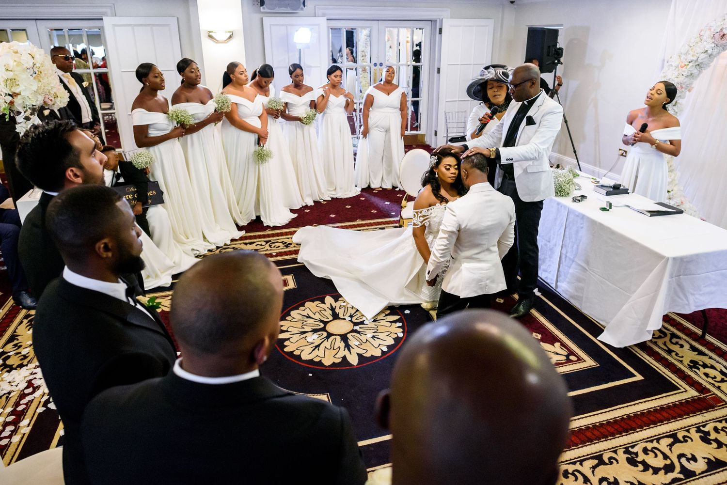 Wedding reception guests gather in elegant venue with decorative carpeting and white decor.