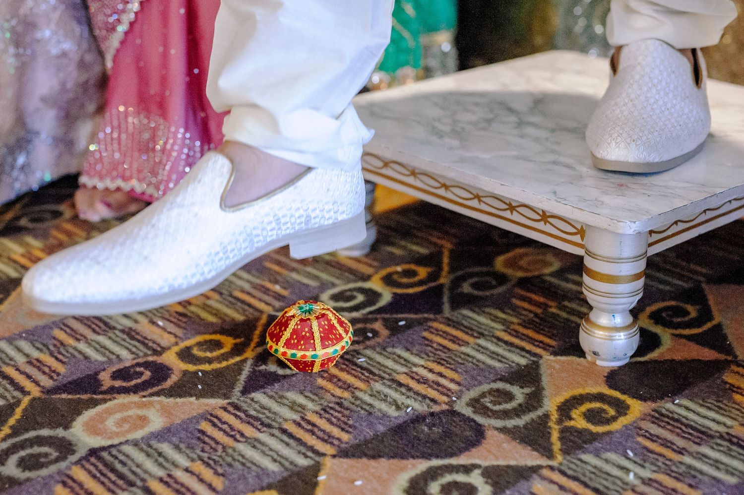 Detailed view of ornate wedding shoes and clothing on a patterned carpet.