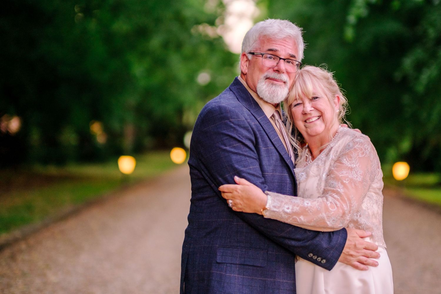 Couple shares romantic moments along a tree-lined path at sunset during their wedding photoshoot.