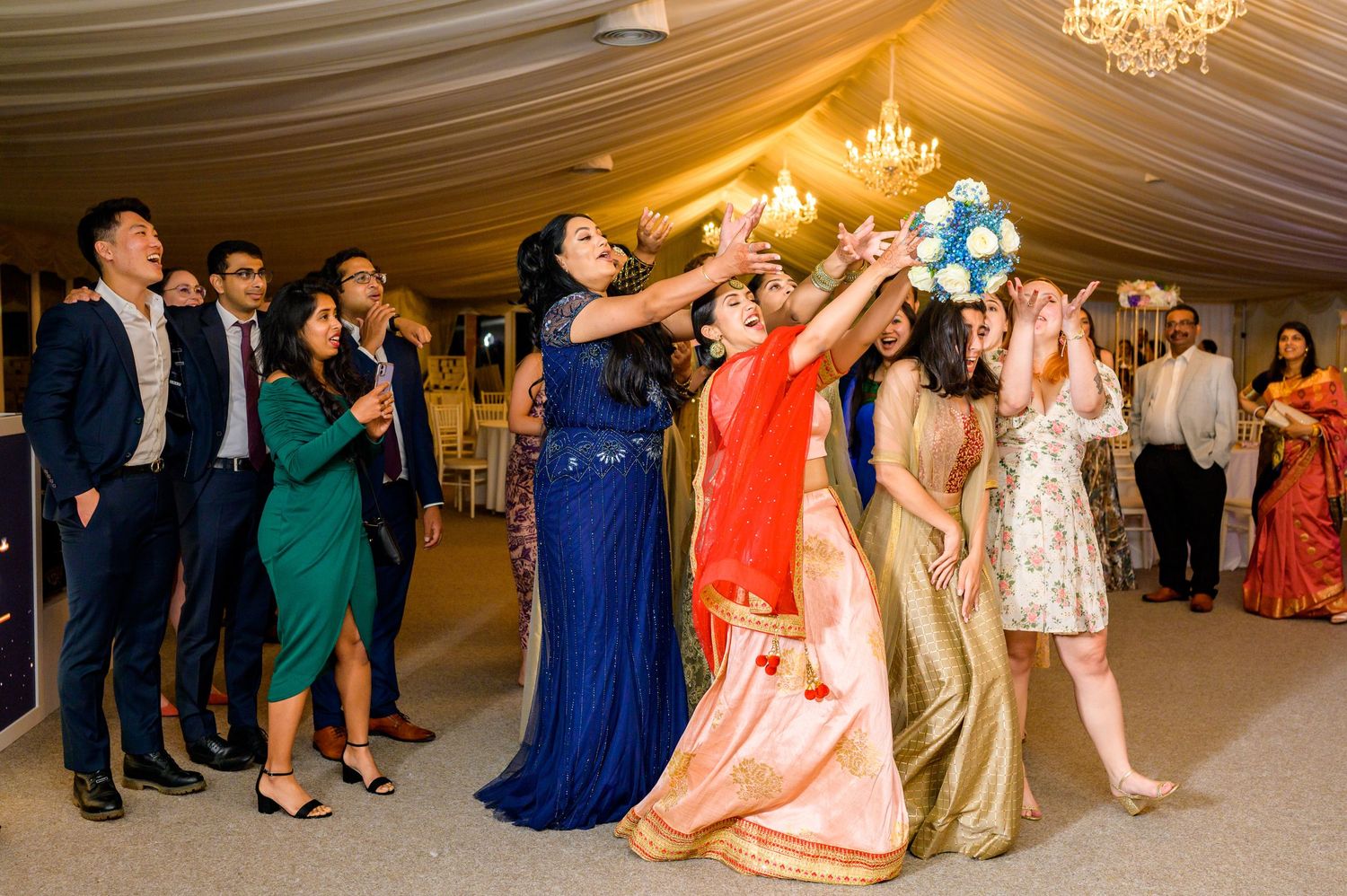 Guests dancing and celebrating at wedding reception in elegantly decorated marquee tent.