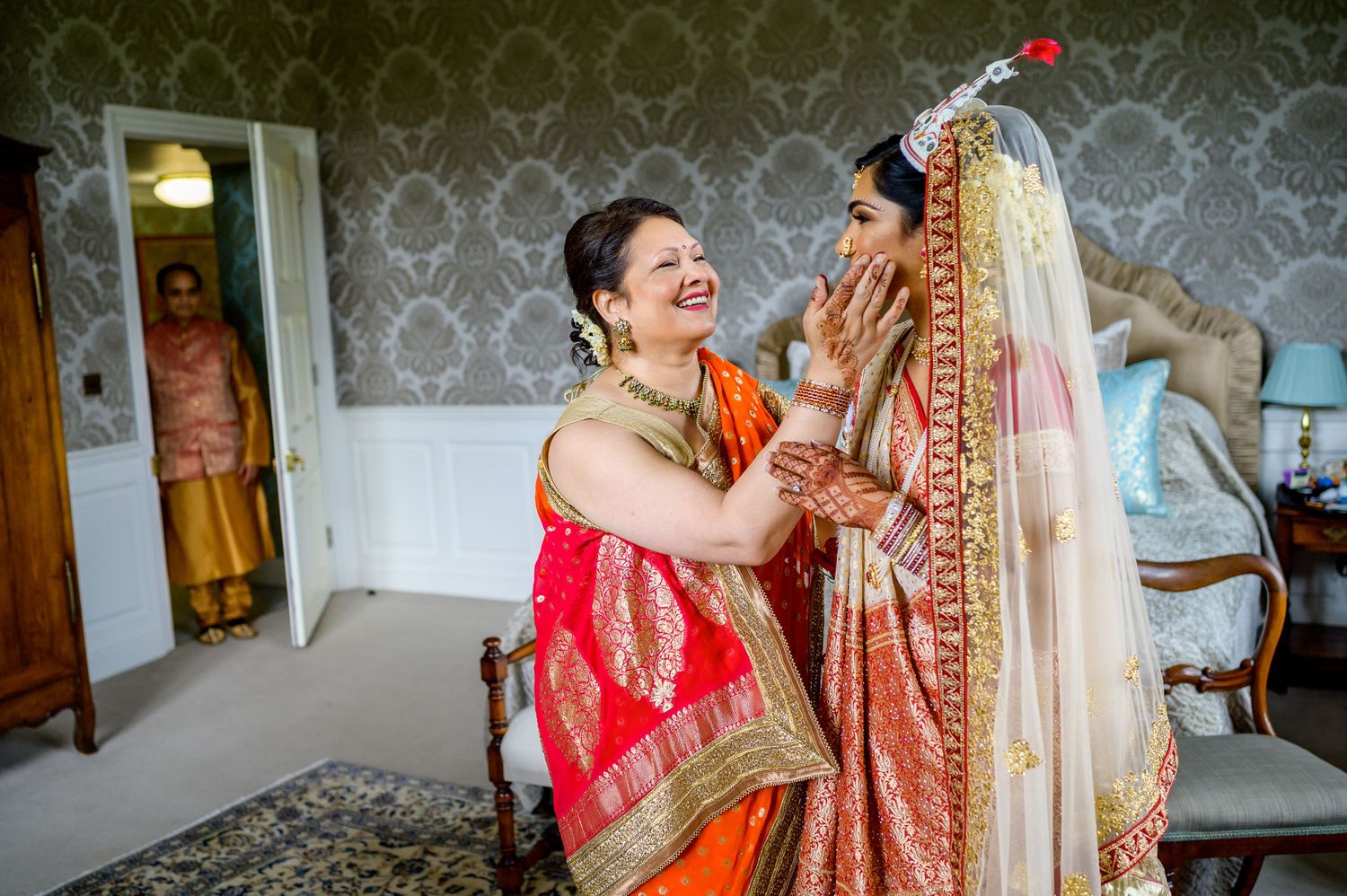 Joyful moment during Indian wedding preparations as attendants help with bridal accessories.