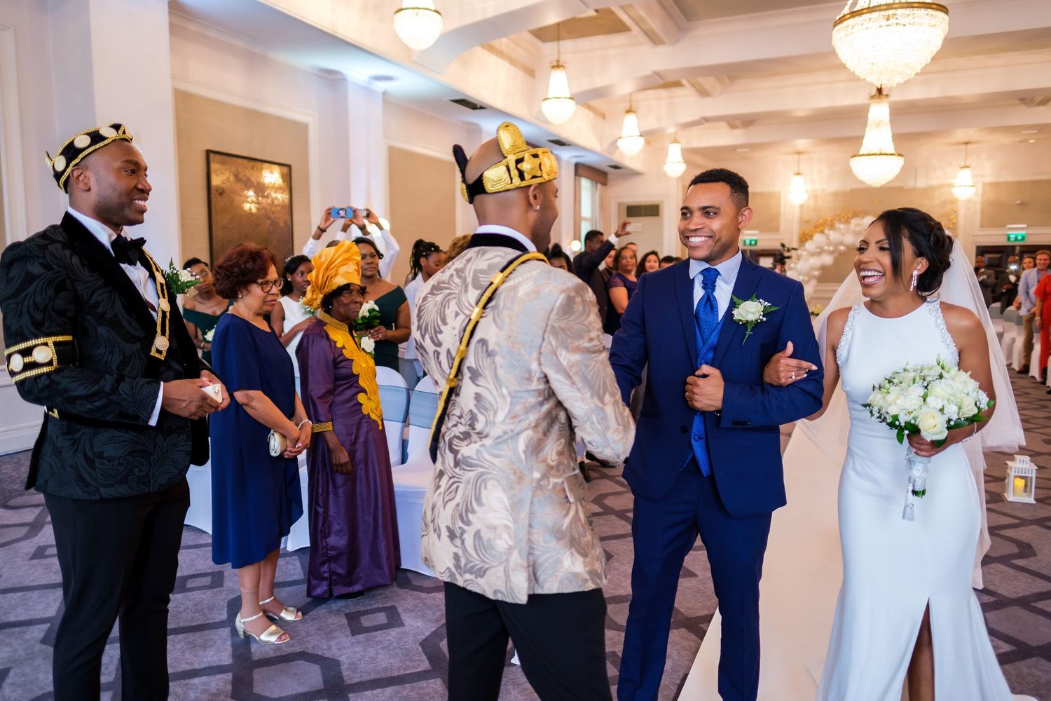 Elegant wedding reception in a grand ballroom with white decor and hanging light fixtures.
