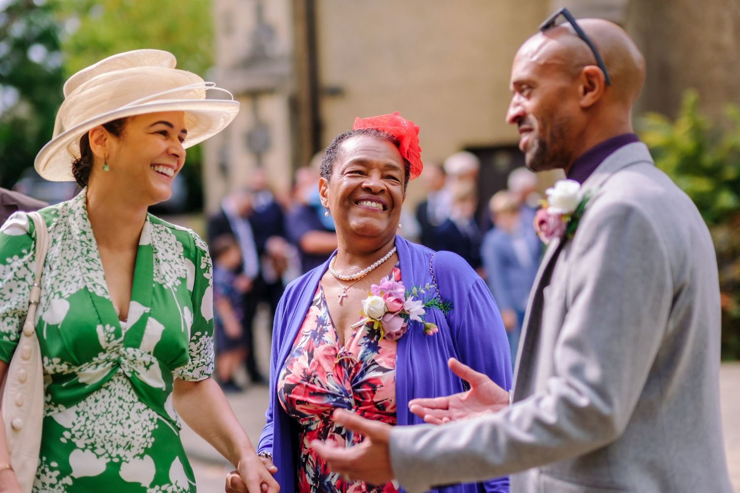 Wedding celebration outdoors with guests in colorful attire mingling near stone architecture.