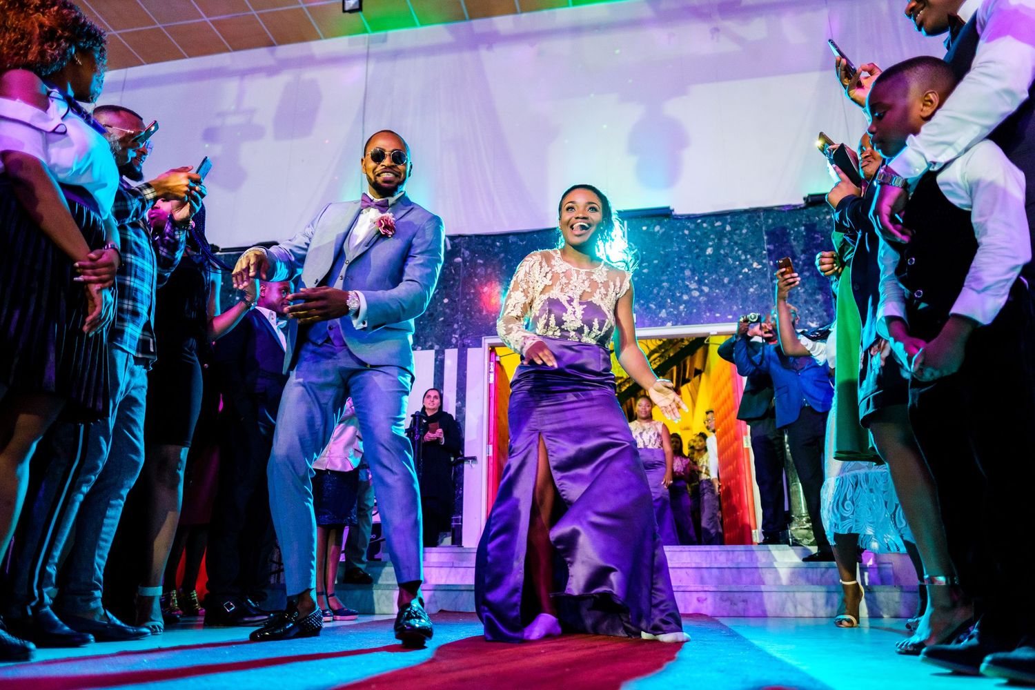 Wedding guests dance under colorful lights at a lively reception party.