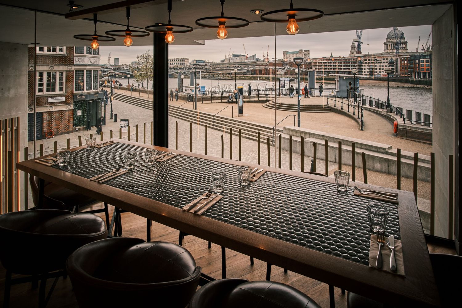 Panoramic view of an empty modern restaurant interior with industrial-style lighting.