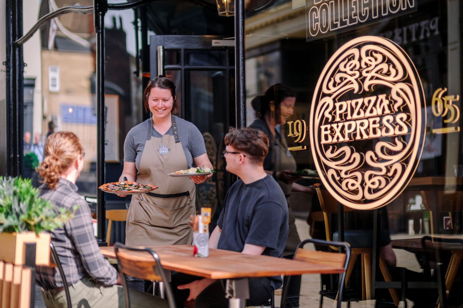 Restaurant diners enjoying meals at outdoor tables with branded signage visible in background.