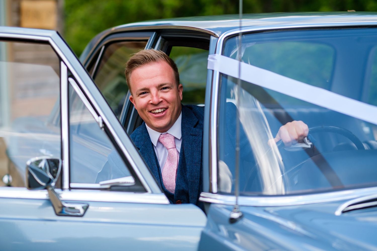Wedding party arrives in classic vintage cars with bright smiles on a sunny day.