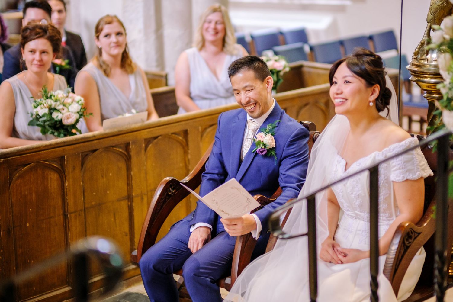 Wedding guests share joyful laughter during a church ceremony while seated in wooden pews.