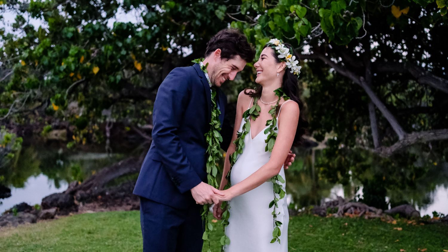 Romantic wedding moment captured under tropical trees by the ocean.