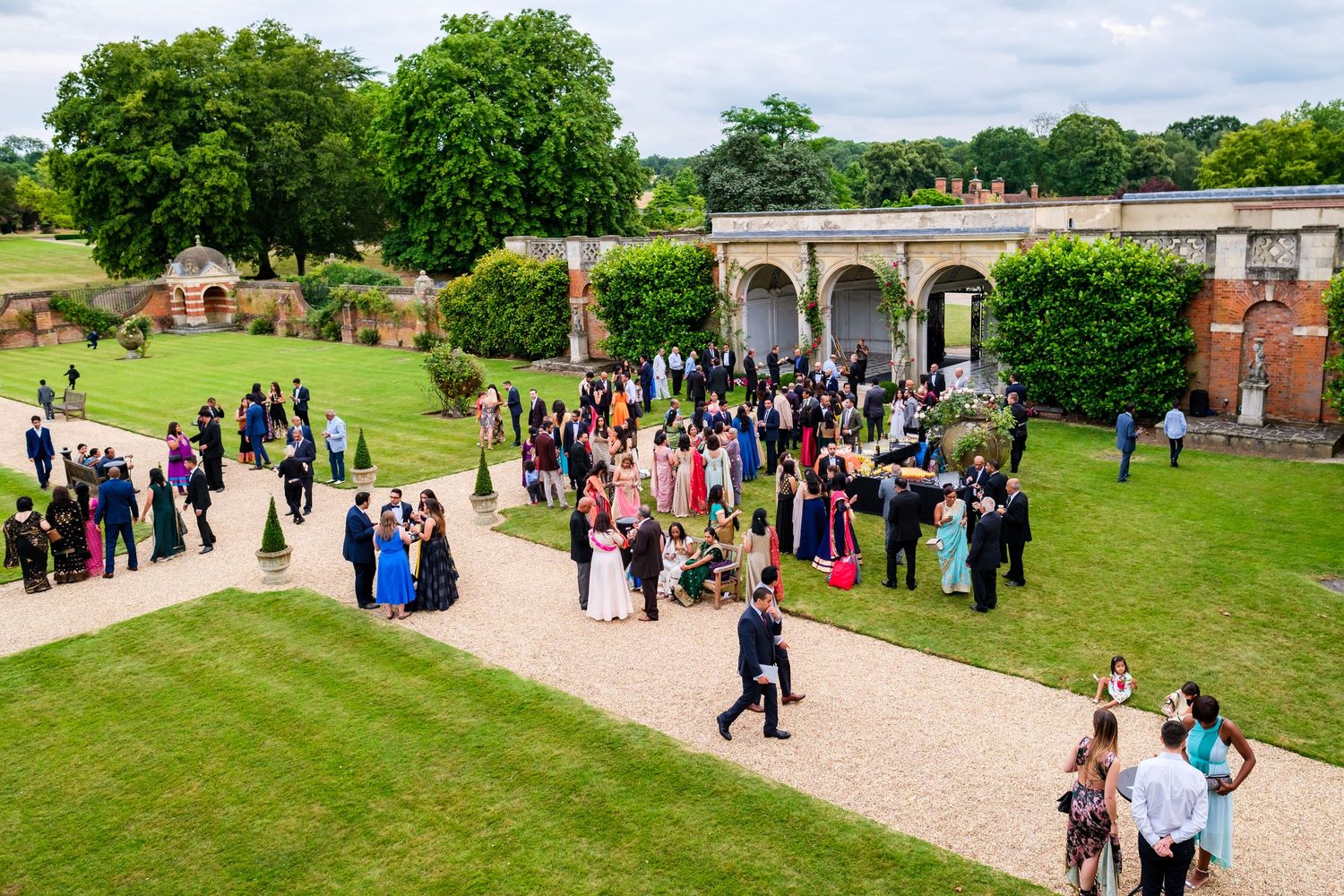 Large group of wedding guests gathered on a sprawling lawn outside a historic venue.