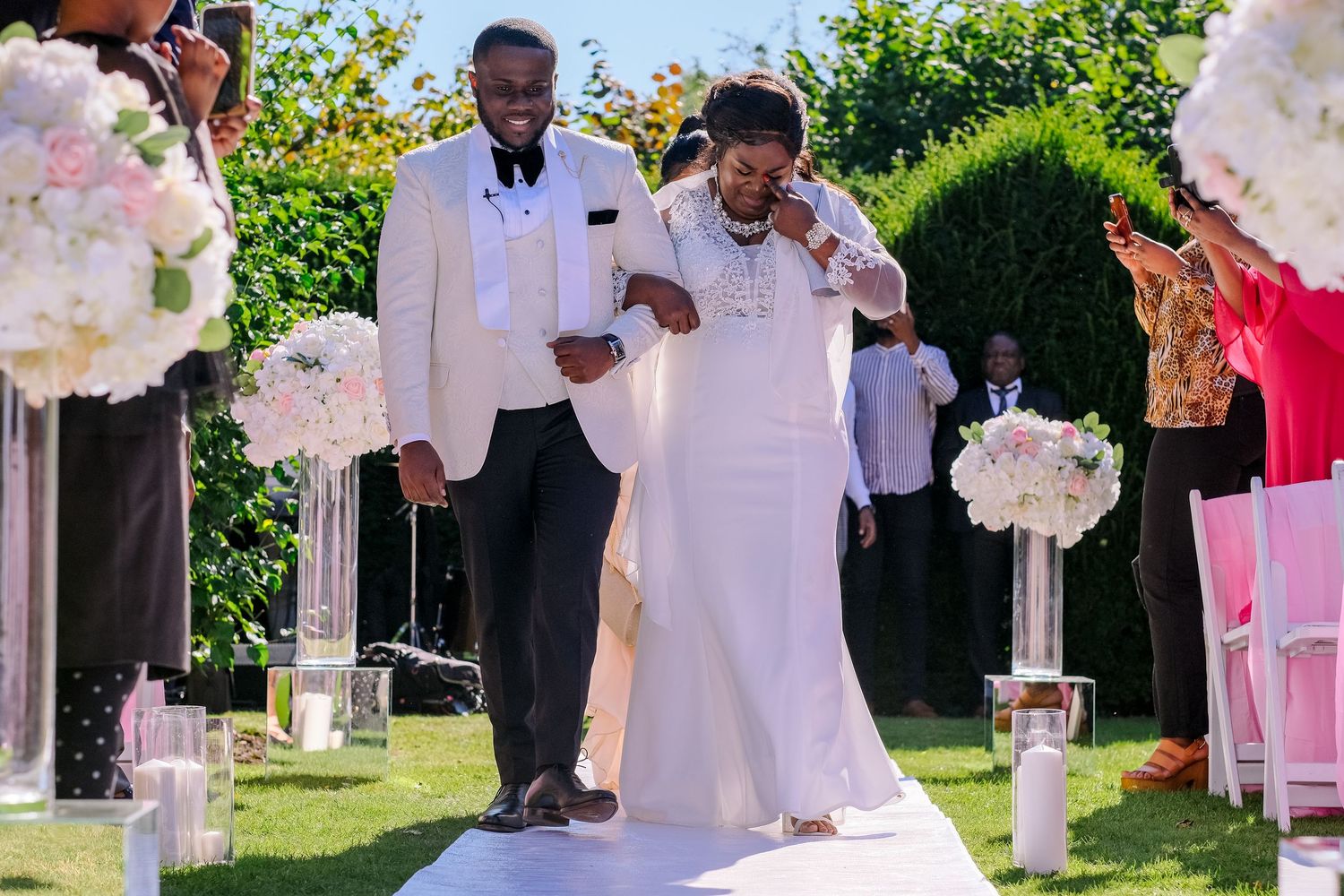 Wedding ceremony setup outdoors with white chairs and floral decorations under sunny skies.