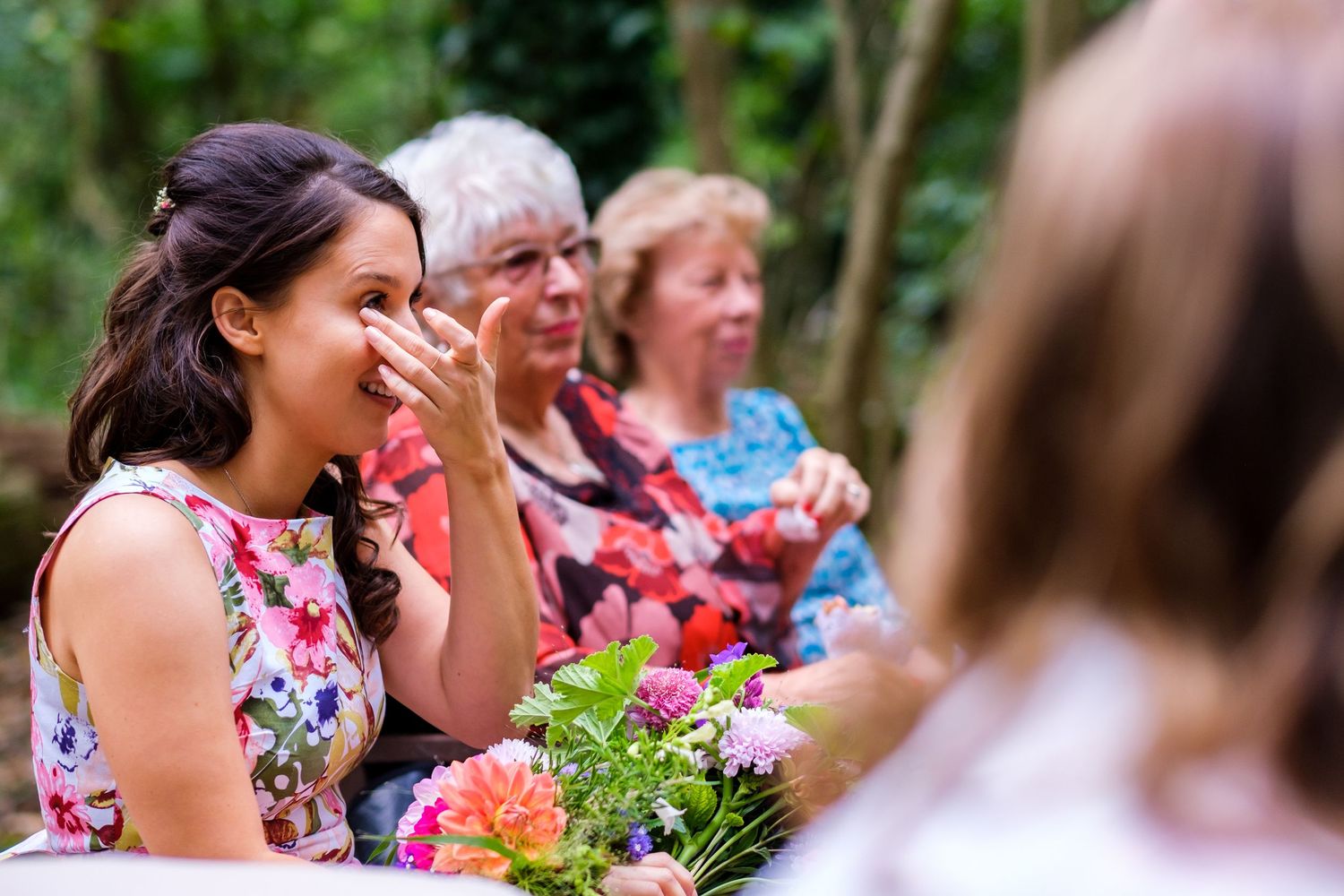 Wedding guests in floral dresses gather outdoors for a summer celebration.