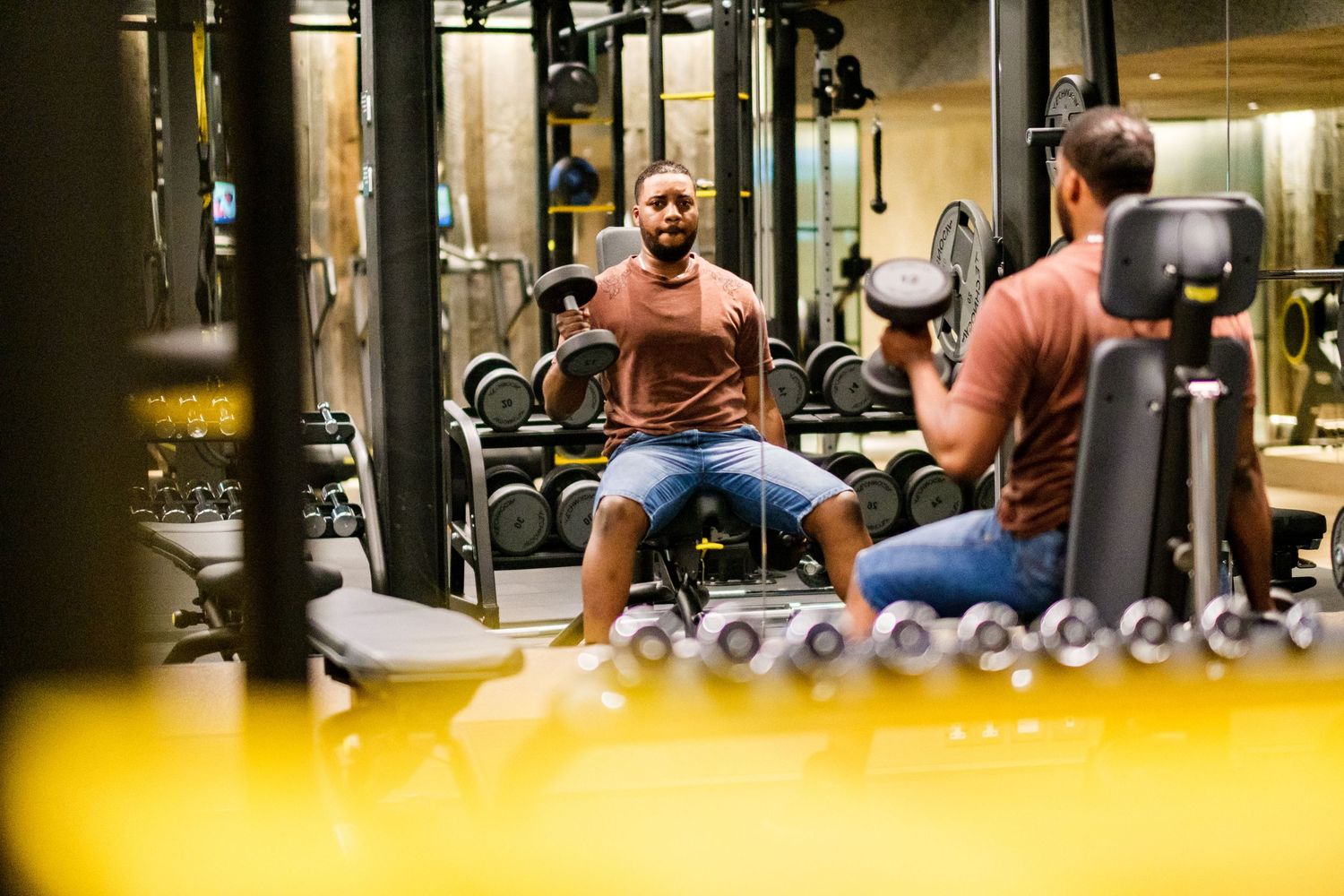 Two people having a conversation while working out in a modern gym with exercise equipment.
