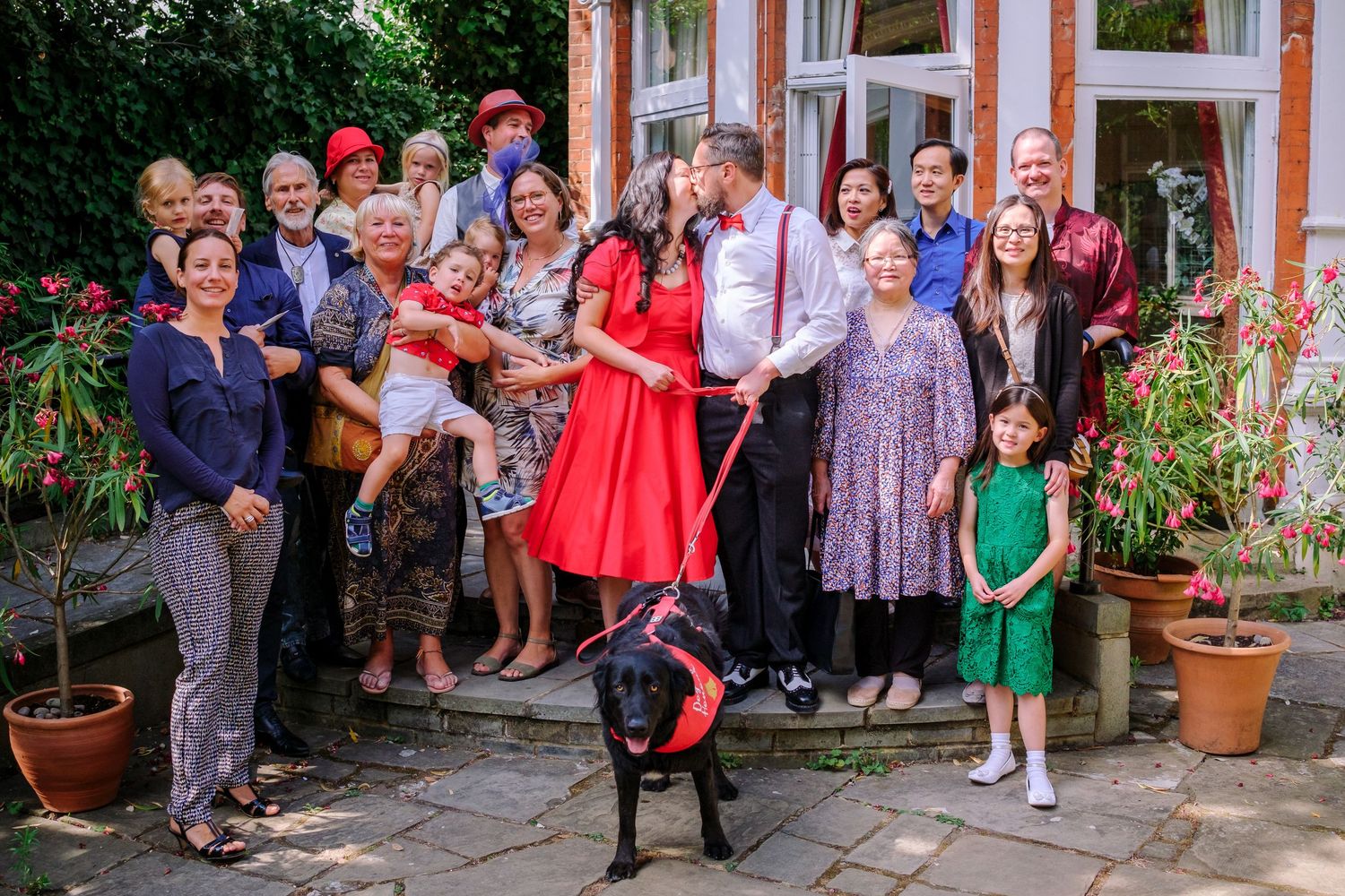A large group of wedding guests gather outside a building in formal attire for a group photograph.