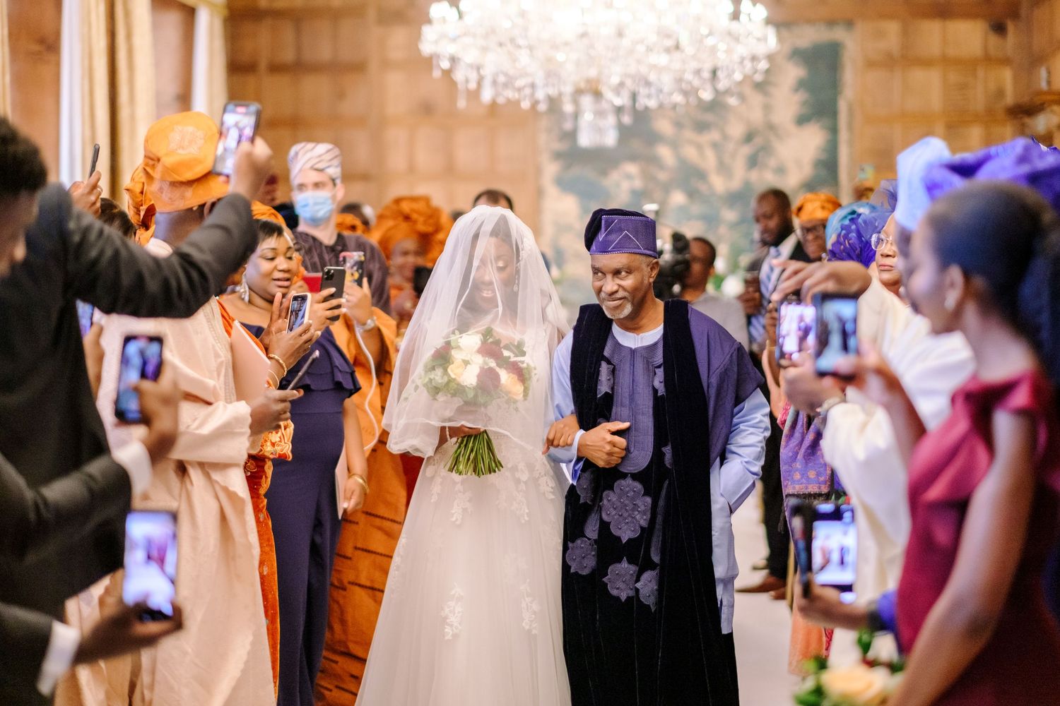 Wedding guests dance and celebrate during a joyful reception under elegant chandeliers.
