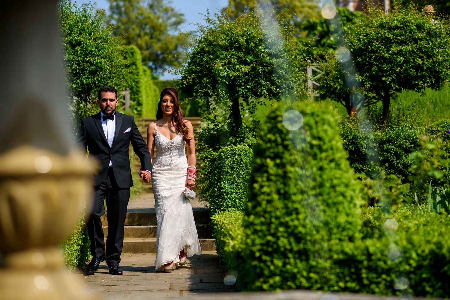 Wedding couple walks through lush garden grounds surrounded by vibrant green landscaping.