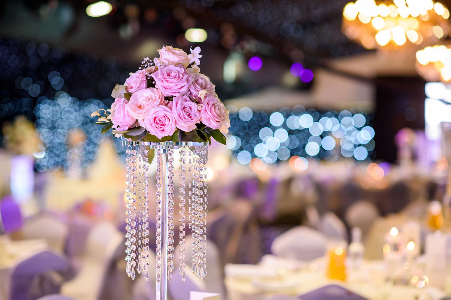 Elegant wedding reception tables with tall floral centerpieces and crystal chandeliers.