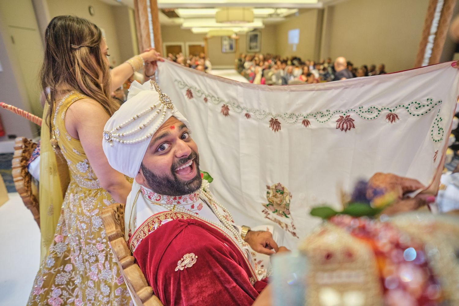 Traditional Indian wedding ceremony with decorative white mandap and guests seated in banquet hall.