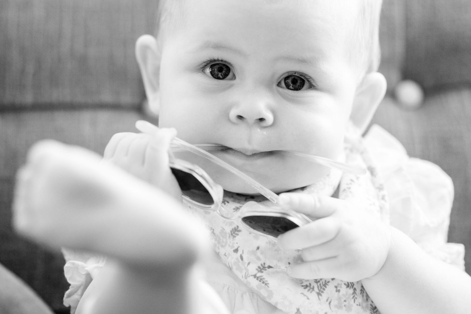 Black and white close-up portrait of a baby in white clothing looking directly at camera.