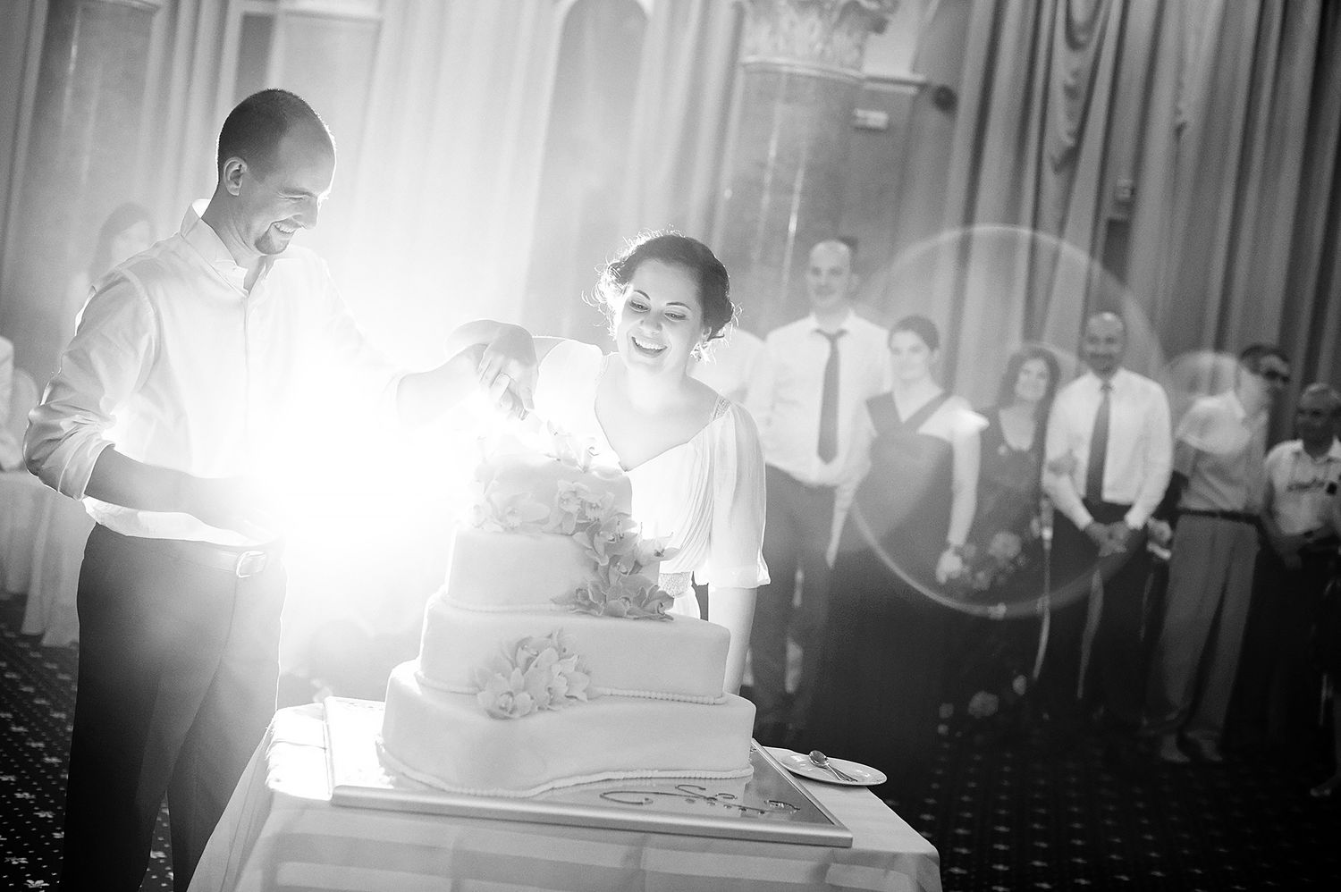 Newlyweds cutting their wedding cake while guests look on at an elegant reception.