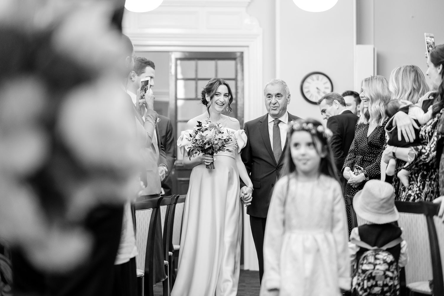 Wedding celebration captured in monochrome showing guests mingling and laughing at an elegant indoor venue.