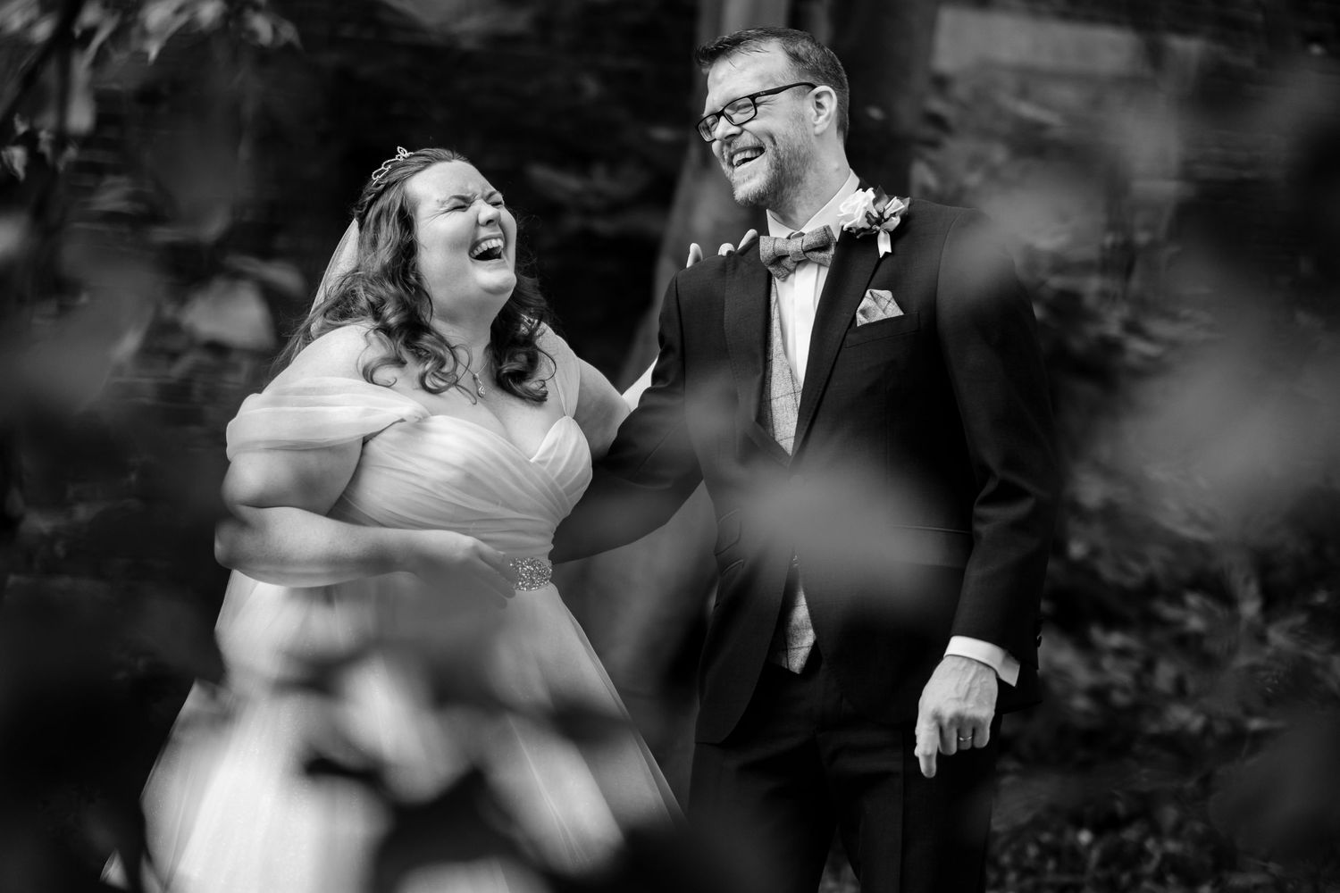 A couple laughs together during a black and white outdoor wedding photoshoot.