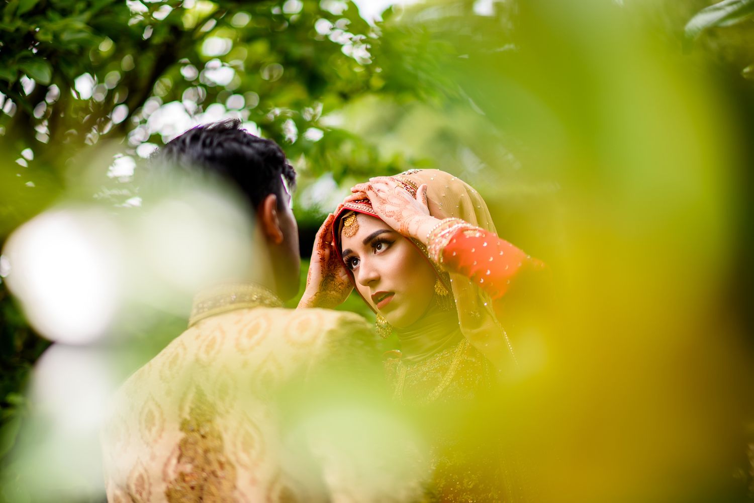 Couple photoshoot through green foliage creating natural framing in outdoor setting.
