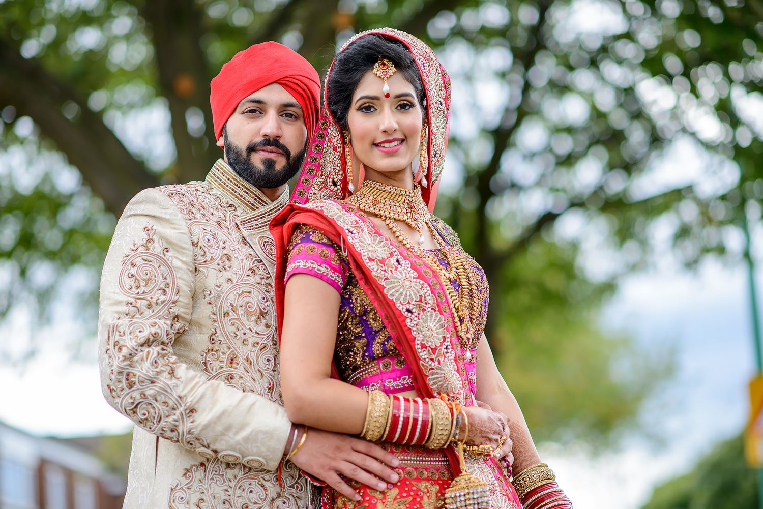 Traditional wedding couple photographed outdoors in red and cream ceremonial attire.