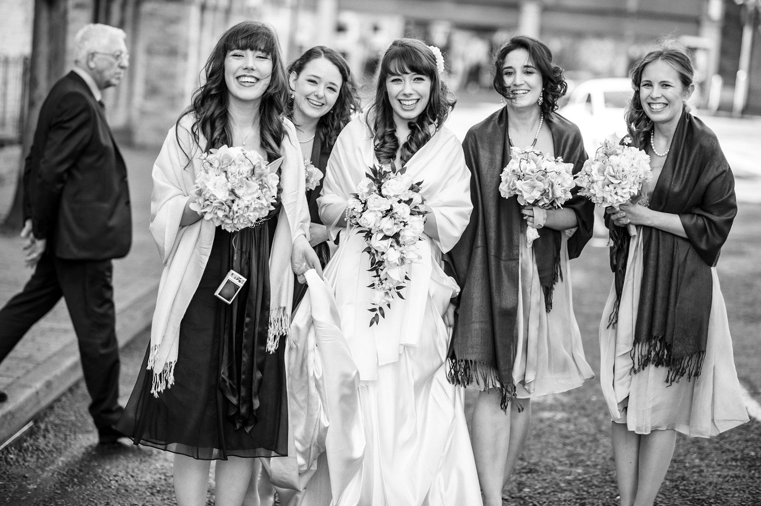 Group wearing winter attire and scarves gathered outdoors for a black and white wedding photo.