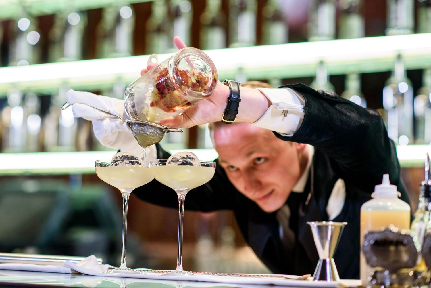 Bartender carefully pouring cocktails into martini glasses with focused precision.