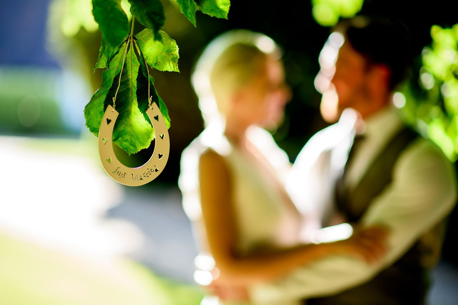 Sunlit green leaves frame an outdoor wedding scene with natural bokeh effects.