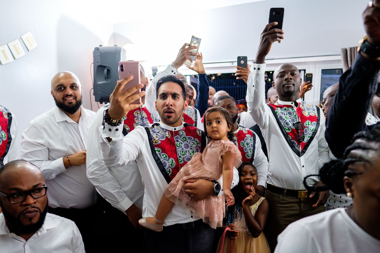 Crowd of people in white shirts raising phones and hands during a celebratory moment.