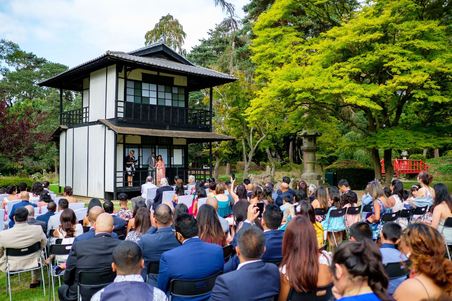 Panoramic view of an outdoor wedding ceremony with Japanese-style architecture and lush green gardens.