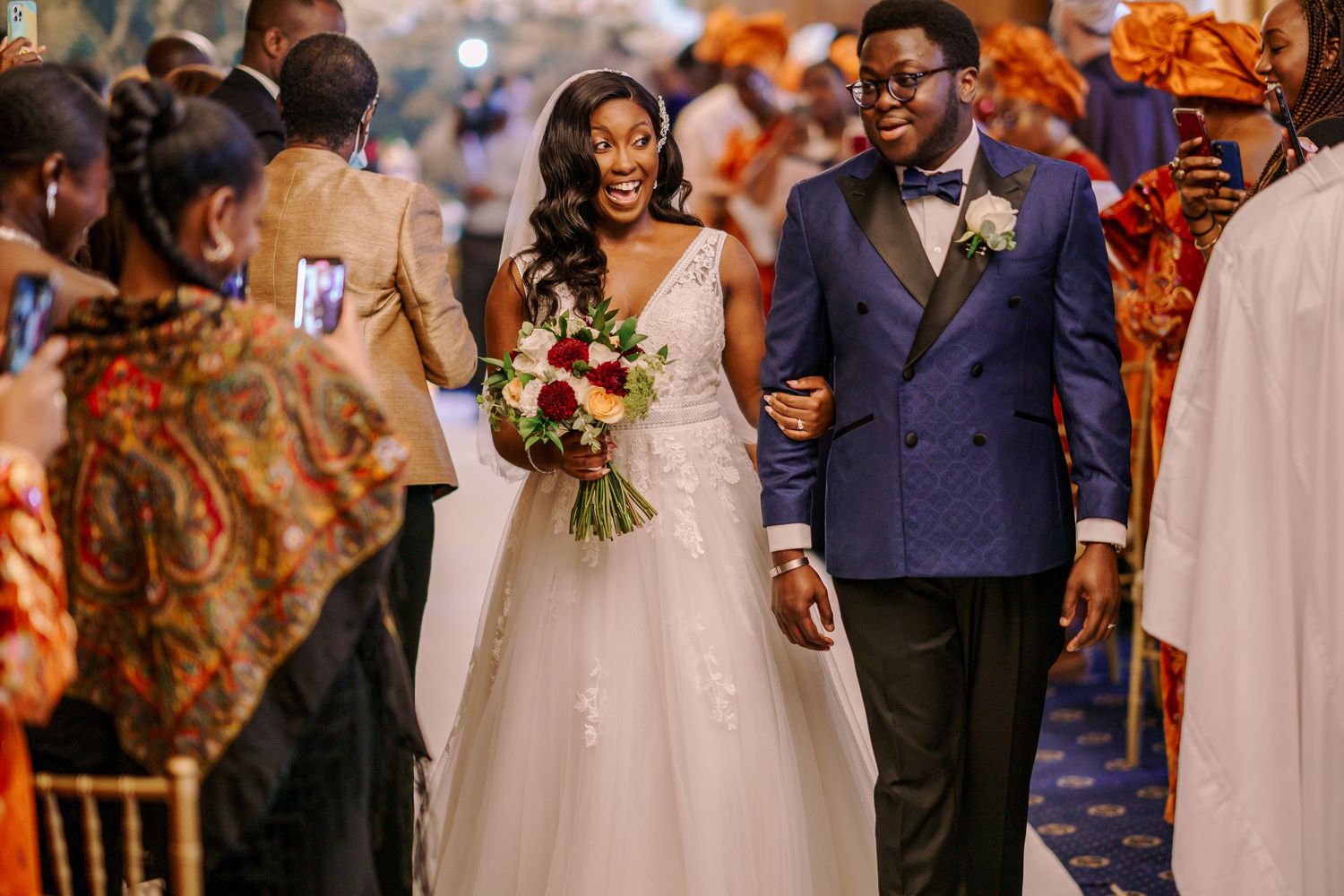 Wedding guests in formal attire gather during reception with warm lighting and festive atmosphere.
