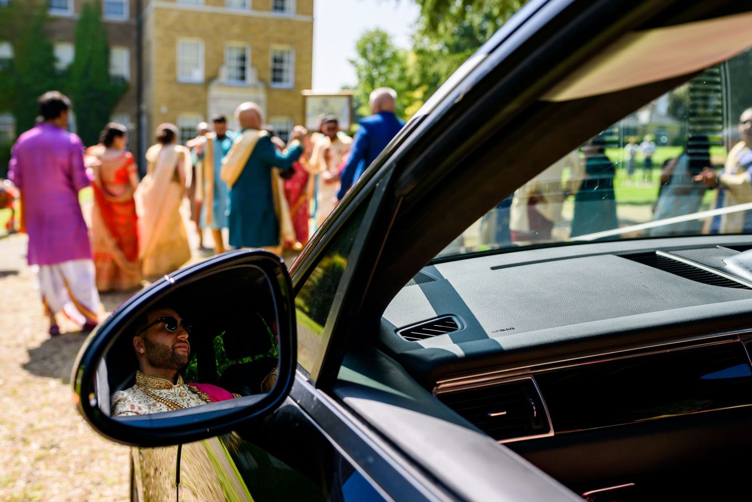 View of car side mirrors and doors on a sunny day with people visible in background.