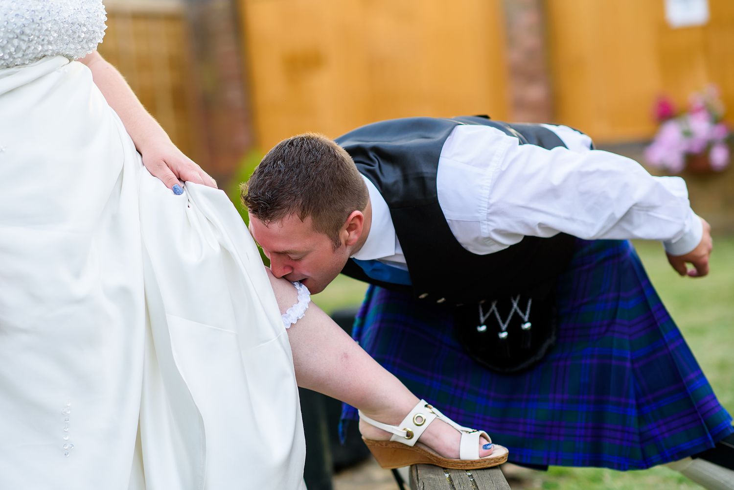 Guests in traditional Scottish kilts dance together at an outdoor wedding celebration.