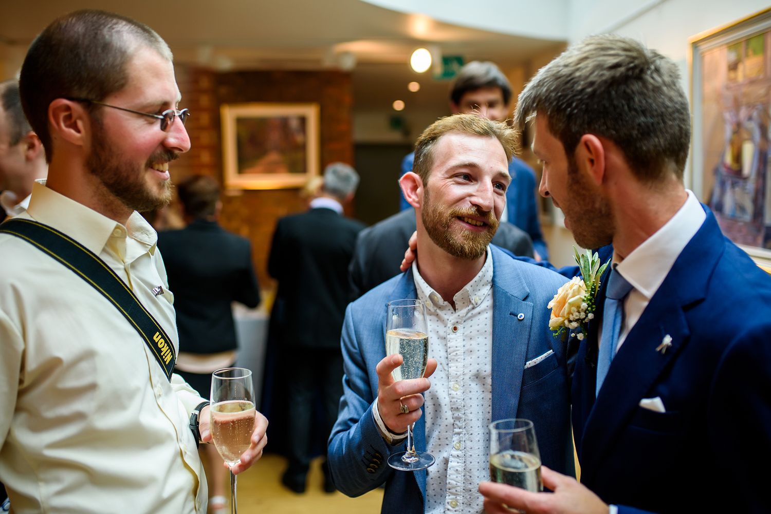 Three guests enjoying drinks and conversation at an indoor wedding reception.