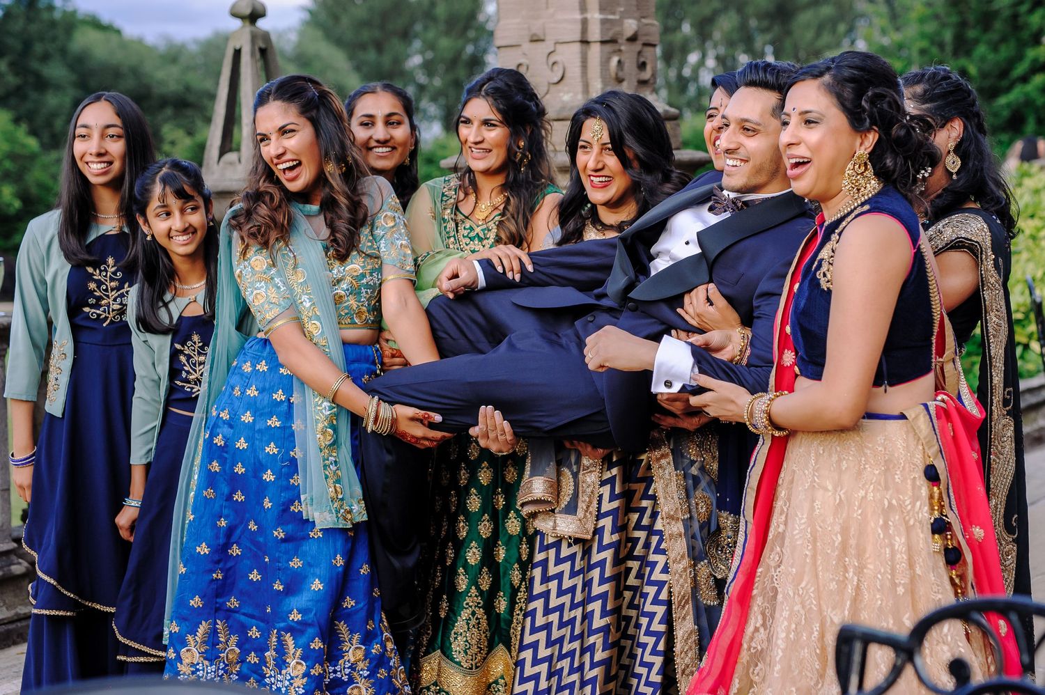 Group of women in colorful traditional Indian attire smiling together outdoors.