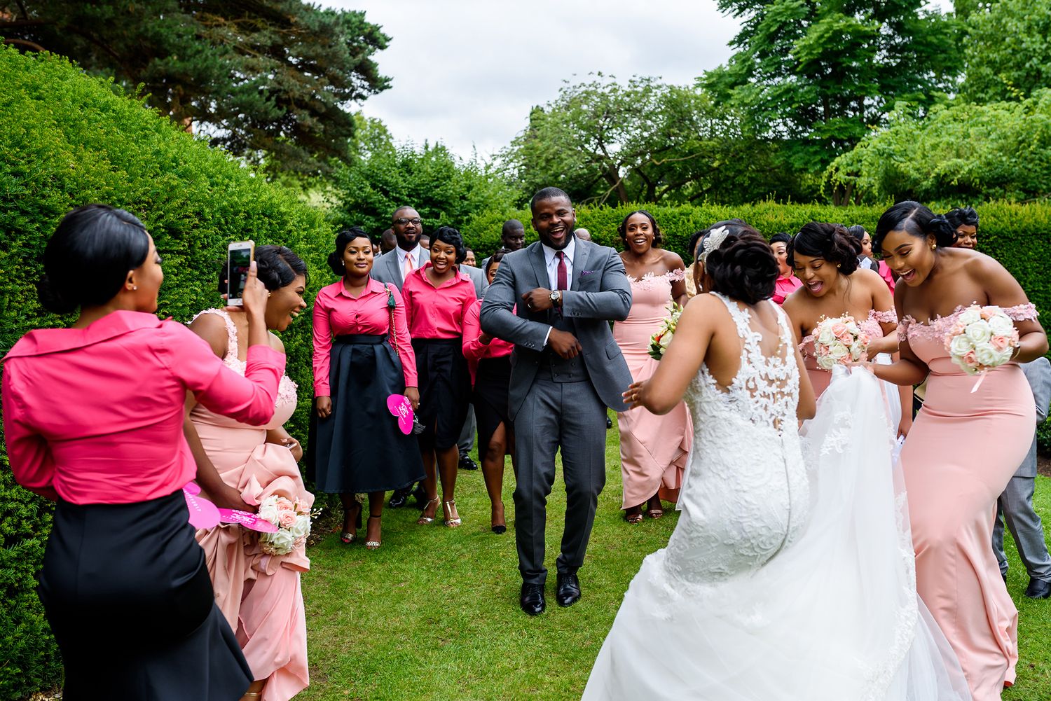 Wedding celebration with bridesmaids in pink dresses dancing in a garden setting.