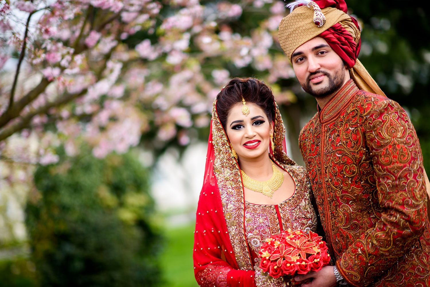 Cherry blossoms frame a couple in traditional South Asian wedding attire.